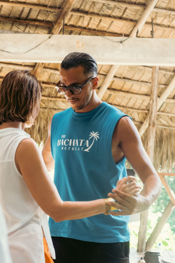 Instructor in a Bachata Retreat shirt dancing with a student in a thatched pavilion